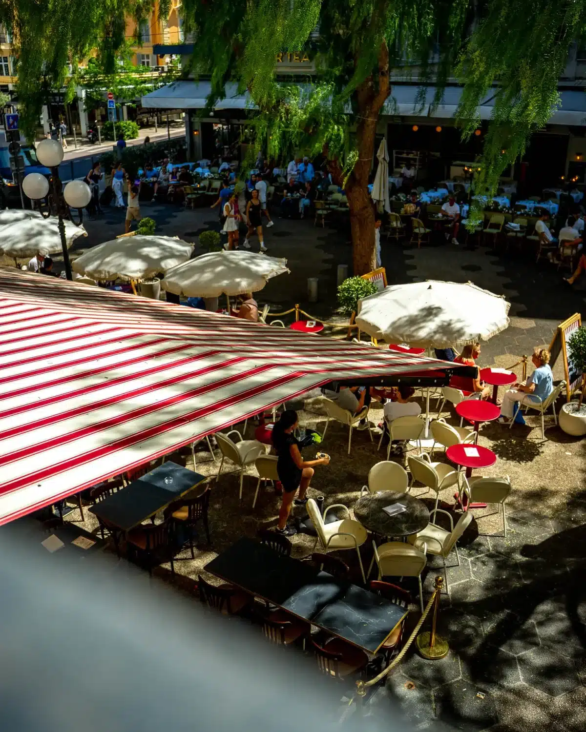 Terrasse animée de NŌVA sous les stores rayés, place Magenta à Nice